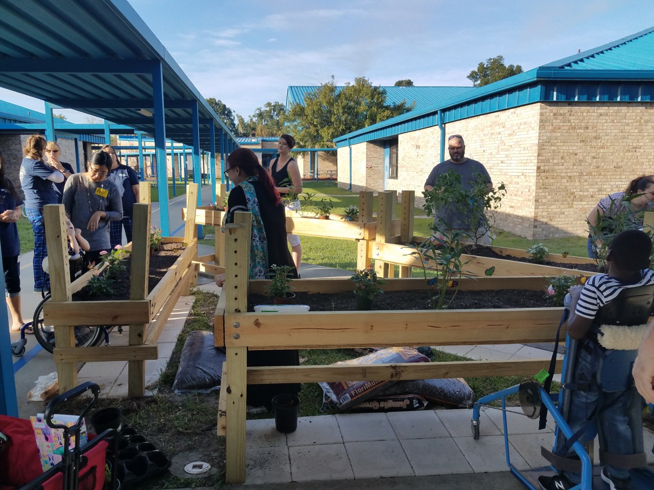 Raised flower beds at an elementary school, several adults waiting to assist children with special need in planting flowers
