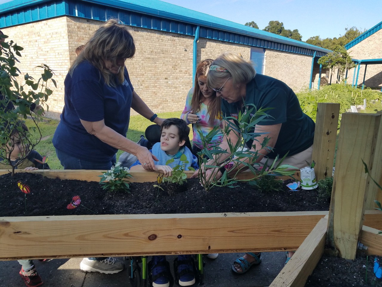 3 adults help a child in a wheelchair plant butterfly-friendly plants in a special raised flower bed